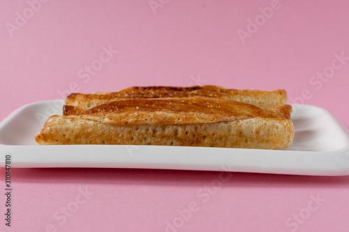 Fried pancakes roll into a tube on a white plate with a pink background.