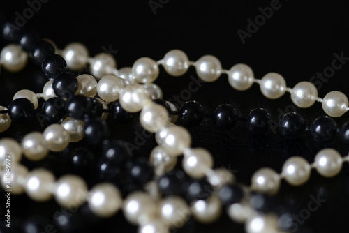 Fragment of a necklace of black and white beads on a black background close-up. Fashion background