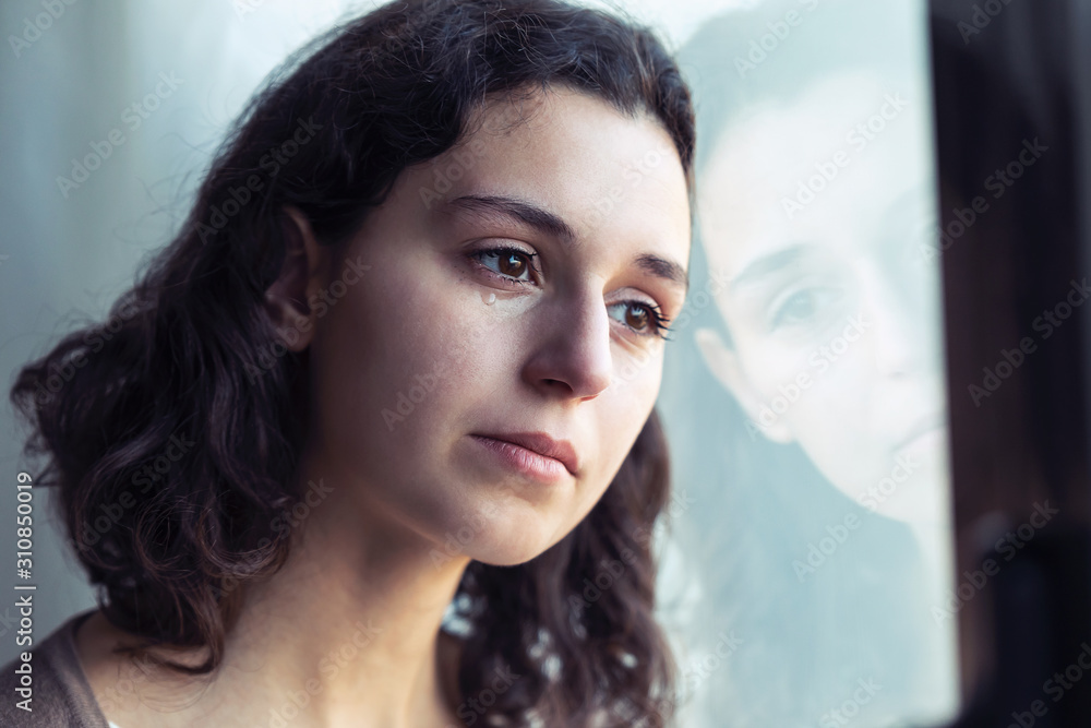 Sad young woman crying while looking through the window at home. Stock ...