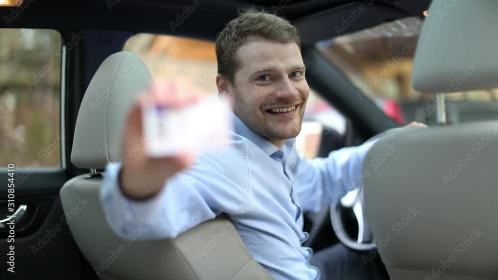 young happy man sitting in the car and showing his new driver license with thumb up sign young happy man sitting in the car and showing his new driver license with thumb up sign