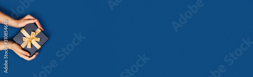 Web-banner with gift box in a female hands on classic blue background. Flat lay, top view, place for text.