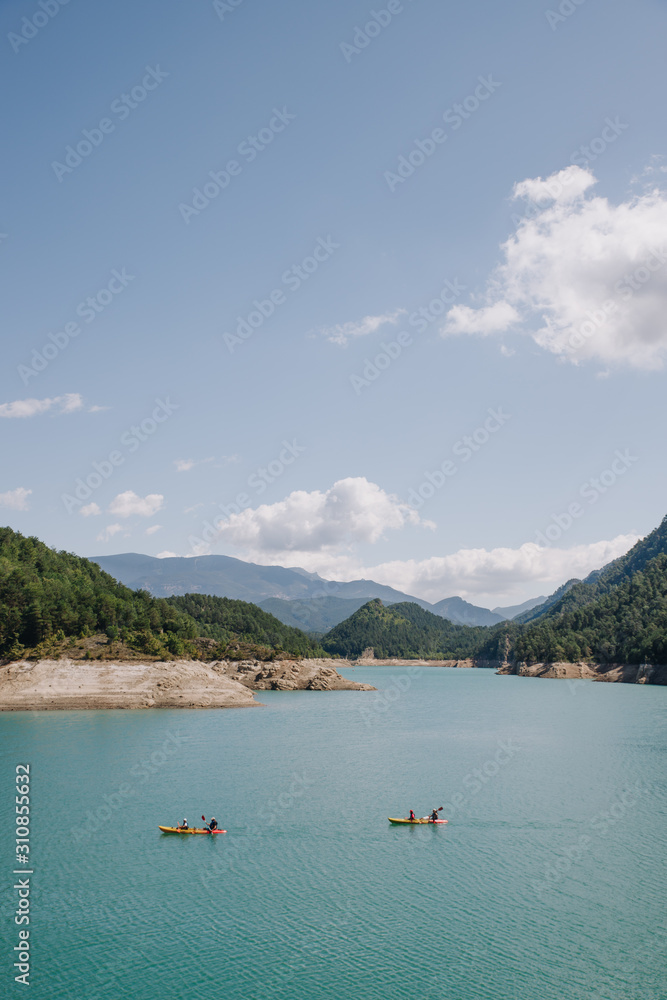 People practicing sport (kayak) on a sunny day in a blue water lake surrounded by mountains on summer