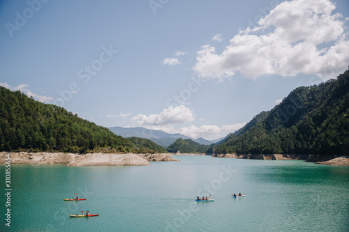 Group of people doing kayak on a blue water lake in the mountains on a sunny day in summer