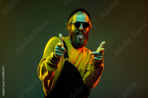 Caucasian woman's portrait on gradient studio background in neon light. Beautiful male model with hipster style in glasses. Concept of human emotions, facial expression, sales, ad. Pointing, choosing.