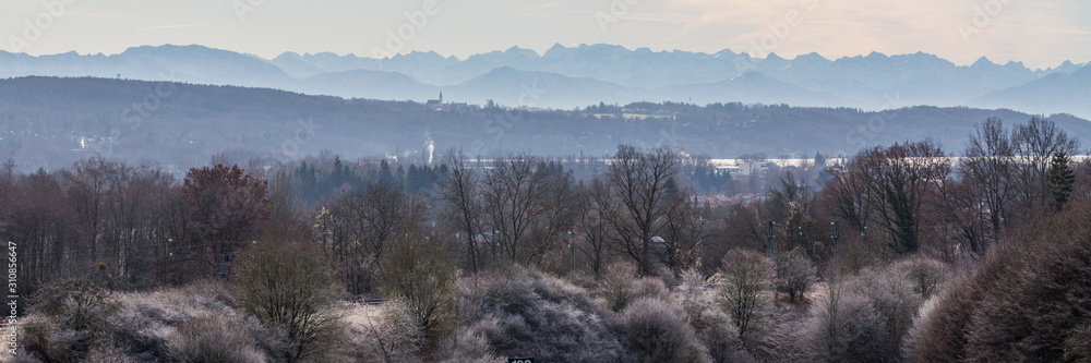 GUT RIEDEN, BAVARIA / GERMANY - December 11, 2019: Panorama of alpine foreland of upper bavaria. Winter landscape with trees in the foreground and the alps in the far distance. Misty and foggy. GUT RIEDEN, BAVARIA / GERMANY - December 11, 2019: Panorama of alpine foreland of upper bavaria. Winter landscape with trees in the foreground and the alps in the far distance. Misty and foggy.