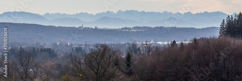 GUT RIEDEN, BAVARIA / GERMANY - December 11, 2019: Panorama of autumn landscape of the alpine foreland close to Lake Starnberg. In the foreground trees, in the far distance the misty bavarian alps. © Chris Redan