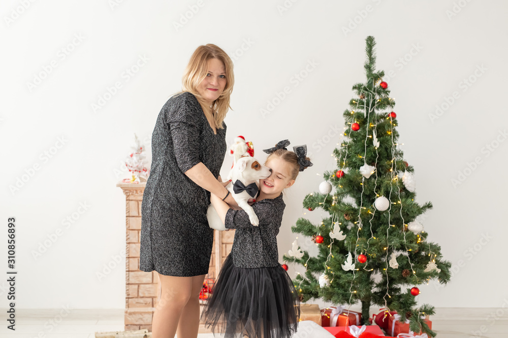 Holidays and pet concept - mother and daughter playing with jack russell terrier dog in front of christmas tree at home Holidays and pet concept - mother and daughter playing with jack russell terrier dog in front of christmas tree at home
