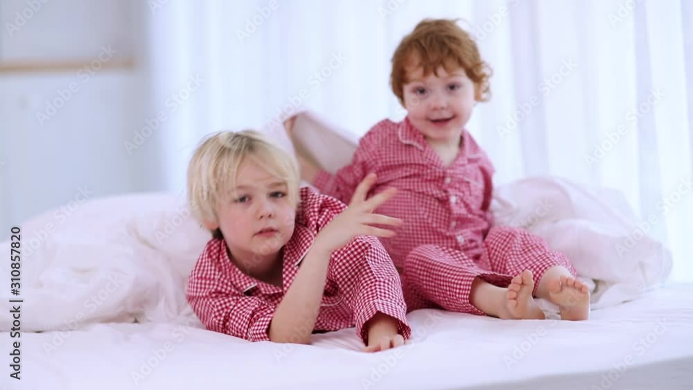 cute siblings in pajamas having fun, hiding under the blanket in bedroom cute siblings in pajamas having fun, hiding under the blanket in bedroom