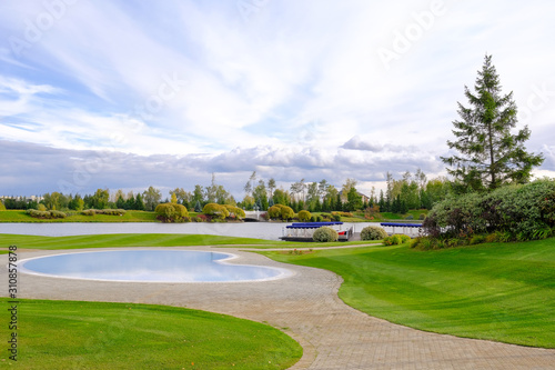 Fototapeta Naklejka Na Ścianę i Meble -  Landscape. View of the beautiful lake and small ornamental ponds covered with paving tiles, lawn with grass, ornamental shrubs and trees, tents and loungers for recreation in the park.