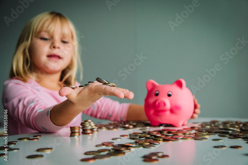 child saving money, cute girl put coins into piggy bank