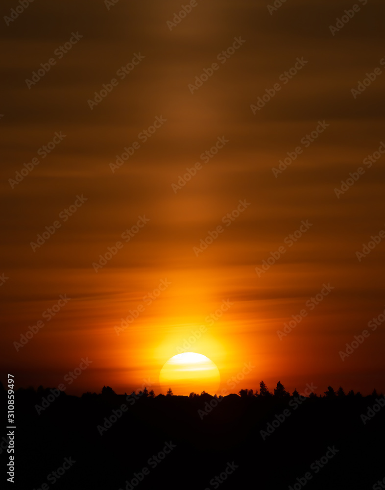 Dramatic sunrise colors as intense yellow sun ball rises over a silhouetted ridge creating an orange streaked sky.