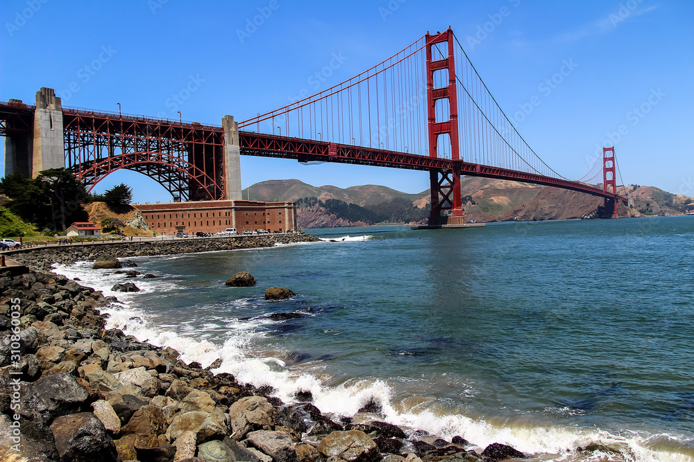 Naklejka premium USA San Francisco June 2018: Photo of the attractions of the Golden Gate Bridge near the water with waves and stones