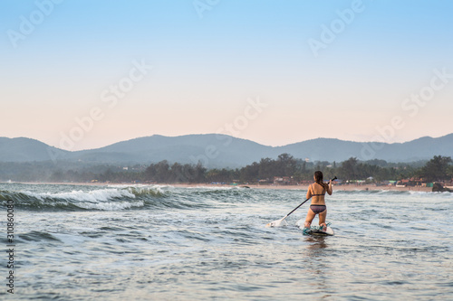 A girl on a stand up paddle board in the ocean at sunset