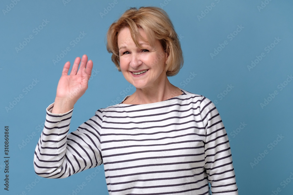 Emotional elderly woman waving hand saying hello on a blue background Emotional elderly woman waving hand saying hello on a blue background