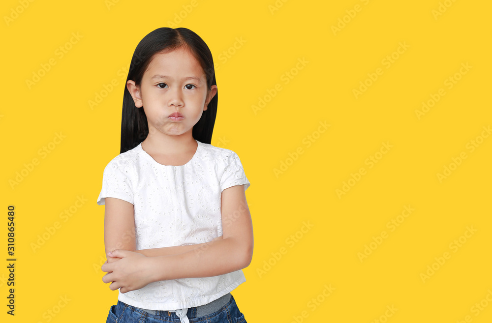Cute little hispanic Asian child girl with arms crossed and angry about something on yellow background with copy space. Person with Negative emotion concept. Cute little hispanic Asian child girl with arms crossed and angry about something on yellow background with copy space. Person with Negative emotion concept.