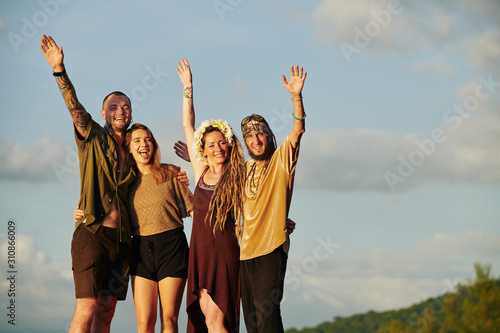 Joyful friends shouting and waving with hands when standing in sunset sun rays