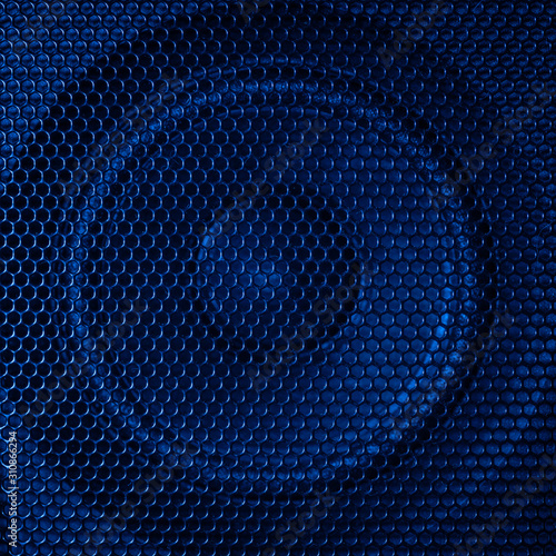 A close up macro photo of a speaker lit with a vibrant blue flash gel