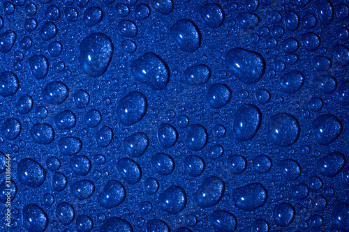 A close up abstract macro photo of water droplets on a grey non stick frying pan material lit with a blue flash gel