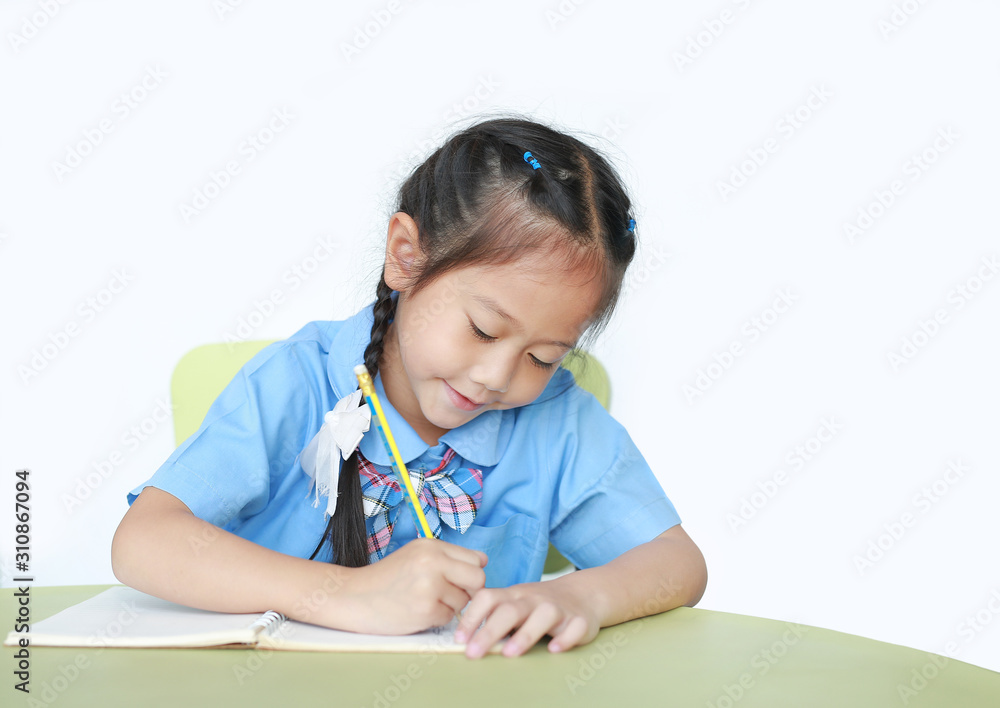 Happy little schoolgirl writing on notebook at desk isolated on white background. Children and Education concept. Happy little schoolgirl writing on notebook at desk isolated on white background. Children and Education concept.
