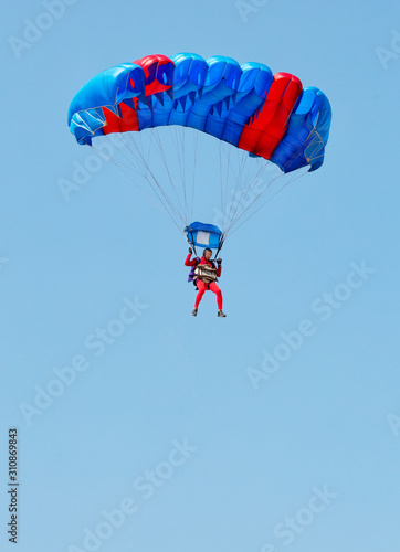 A paratrooper in a red suit descends under the canopy of a parachute