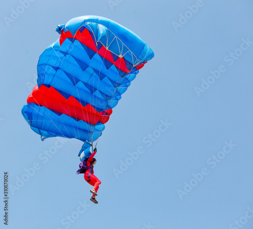 Paratrooper in red suit descends under canopy of parachute Fototapet