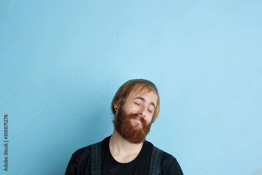 Obraz premium Portrait of young caucasian man looks dreamful, cute and happy. Looking up and thinking on blue studio background. Copyspace for your advertising. Concept of future, target, dreams, visualisation.