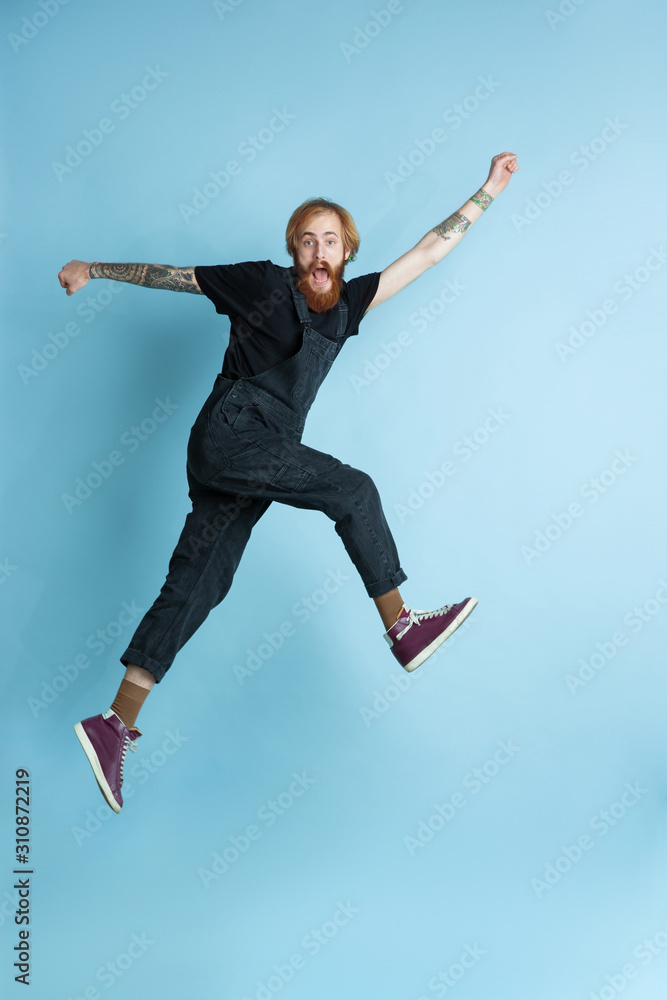 Portrait of young caucasian man looks dreamful, cute and happy. Jumping. laughting on blue studio background. Copyspace for your advertising. Concept of future, target, dreams, visualisation.
