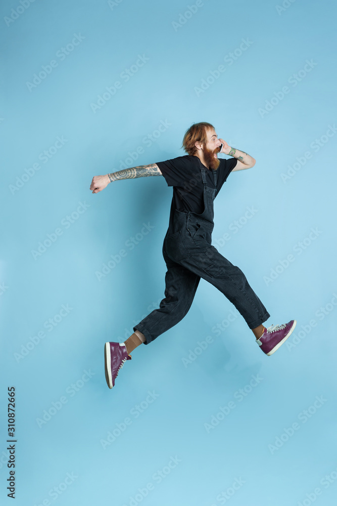 Fototapeta Portrait of young caucasian man looks dreamful, cute and happy. Jumping. laughting on blue studio background. Copyspace for your advertising. Concept of future, target, dreams, visualisation.