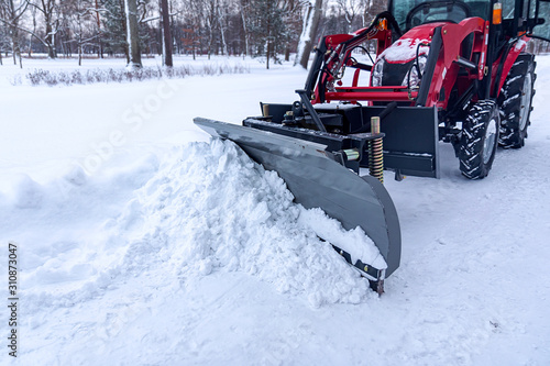 red tractor removes snow with a bucket from a road in a park