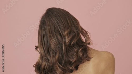 Back view of half-naked woman is shaking her hair with hands isolated over pink background photo