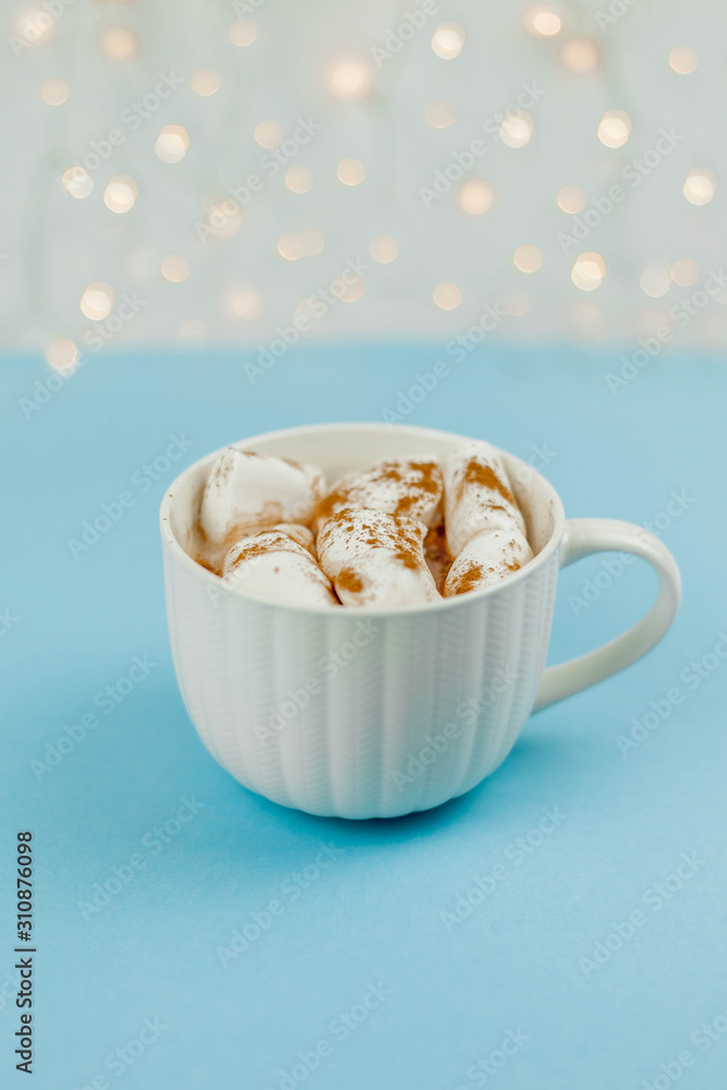 A large white mug with cocoa and marshmallows, cinnamon on a blue background. Christmas motives. Traditional winter drink. A large white mug with cocoa and marshmallows, cinnamon on a blue background. Christmas motives. Traditional winter drink.