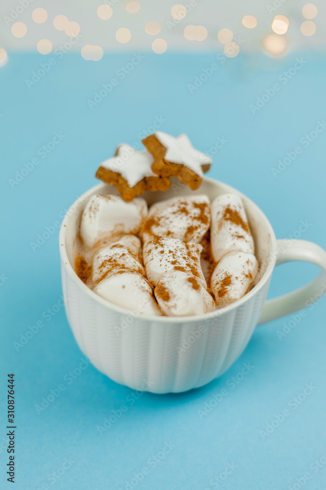 A large white mug with cocoa and marshmallows, cinnamon on a blue background. Christmas cookies. Traditional winter drink.