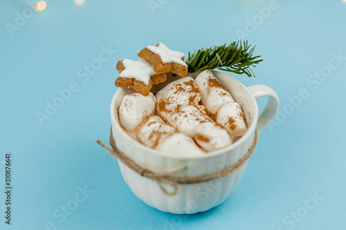 A large white mug with cocoa and marshmallows, cinnamon on a blue background. Christmas cookies. Traditional winter drink.