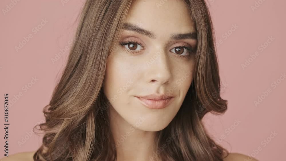 A close-up view of young calm attractive woman is looking to the camera and smiling isolated over pink background A close-up view of young calm attractive woman is looking to the camera and smiling isolated over pink background