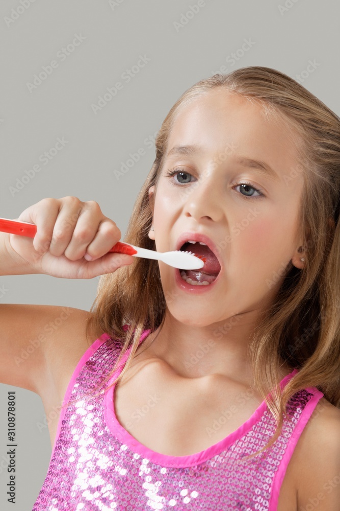 Young girl brushing teeth against gray background Young girl brushing teeth against gray background