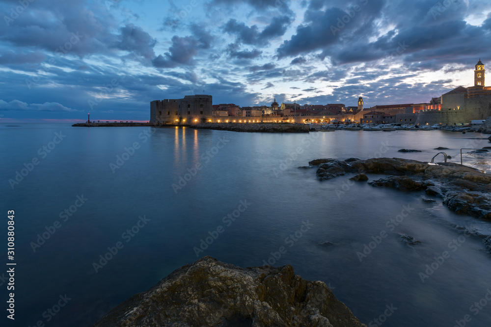 Sunset and Night view of Dubrovnik old town from seaside with reefs in foreground, Croatia