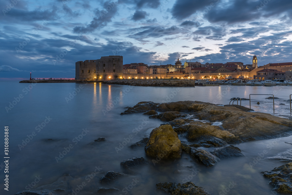 Sunset and Night view of Dubrovnik old town from seaside with reefs in foreground, Croatia