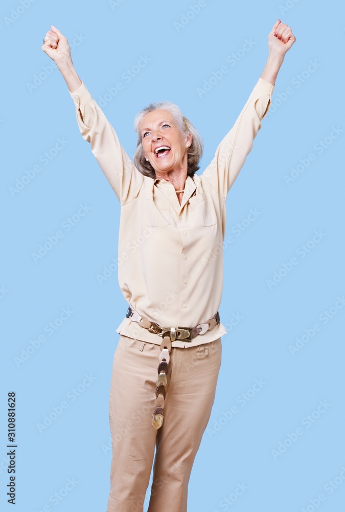 Excited senior woman in casuals cheering with arms raised against blue background Excited senior woman in casuals cheering with arms raised against blue background