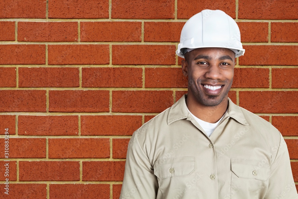 Portrait of happy young construction worker with hardhat over brick wall Portrait of happy young construction worker with hardhat over brick wall