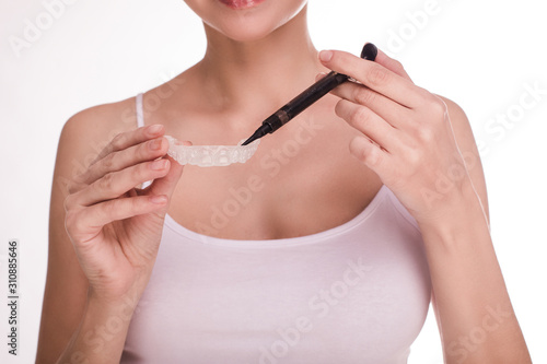 Cut view of woman put some whitening gel in kappa for teeth. Getting ready to procedure. Take oral care. Young slim woman hold whitening pen gel in hand. Isolated over white background.