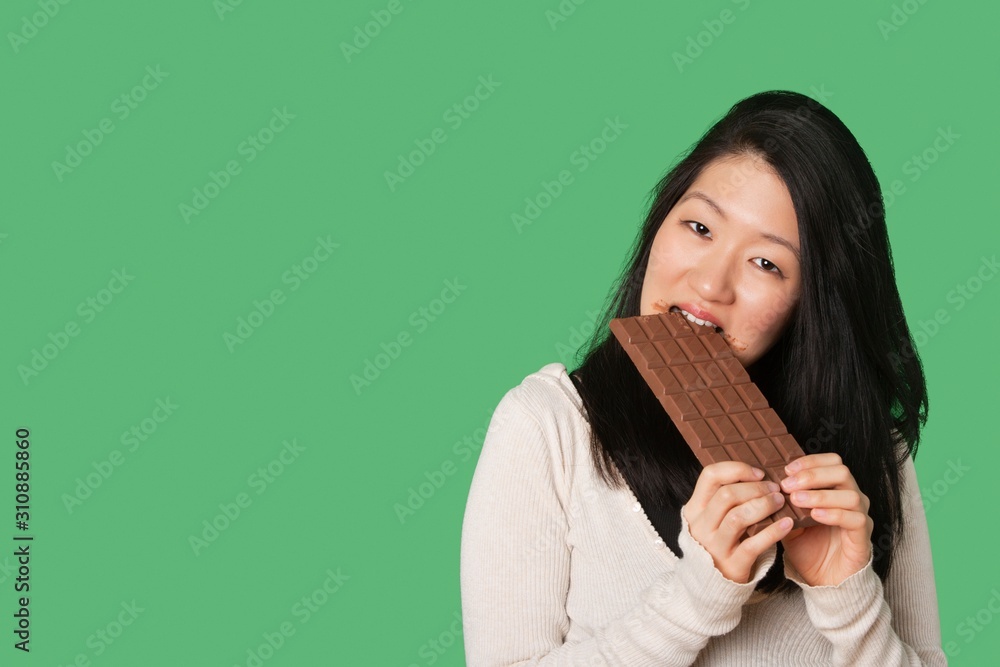 Portrait of a young woman eating a large chocolate bar over green background Portrait of a young woman eating a large chocolate bar over green background