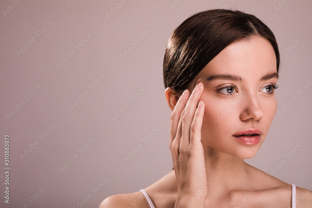 Portrait of young woman hold fingers of one hand close to head. Look to right. worried about headache or pain. Isolated over beige background. Portrait of young woman hold fingers of one hand close to head. Look to right. worried about headache or pain. Isolated over beige background.