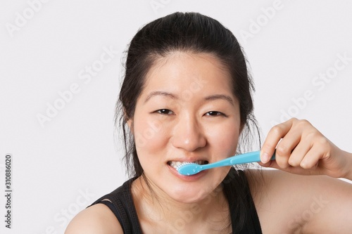 Portrait of a young woman brushing her teeth over light gray background