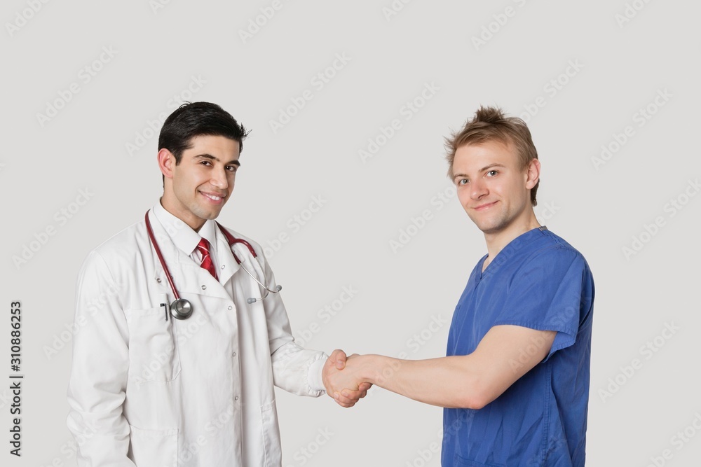 Portrait of doctor and male nurse shaking hands over gray background Portrait of doctor and male nurse shaking hands over gray background