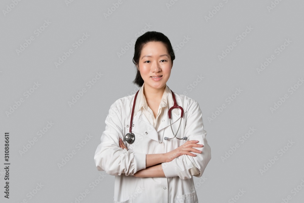 Portrait of an Asian female doctor standing with arms crossed over gray background Portrait of an Asian female doctor standing with arms crossed over gray background
