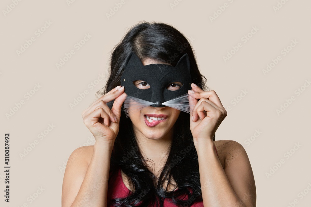 Portrait of a young woman wearing eye mask while biting lip over colored background Portrait of a young woman wearing eye mask while biting lip over colored background