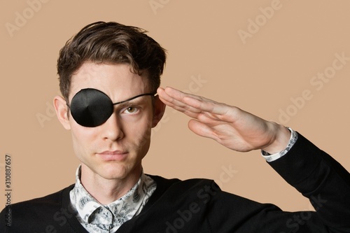 Portrait of a man wearing eye patch saluting over colored background photo