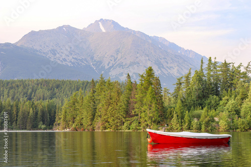 Red boat on a lake in the mountains. High Tatras mountains on a sunny day. Boat, lake, forest, mountains.