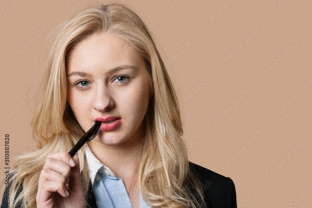 Portrait of a blond business woman with pen in mouth over colored background Portrait of a blond business woman with pen in mouth over colored background
