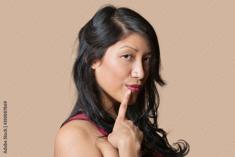 Portrait of a beautiful young woman posing with finger on lip over colored background Portrait of a beautiful young woman posing with finger on lip over colored background